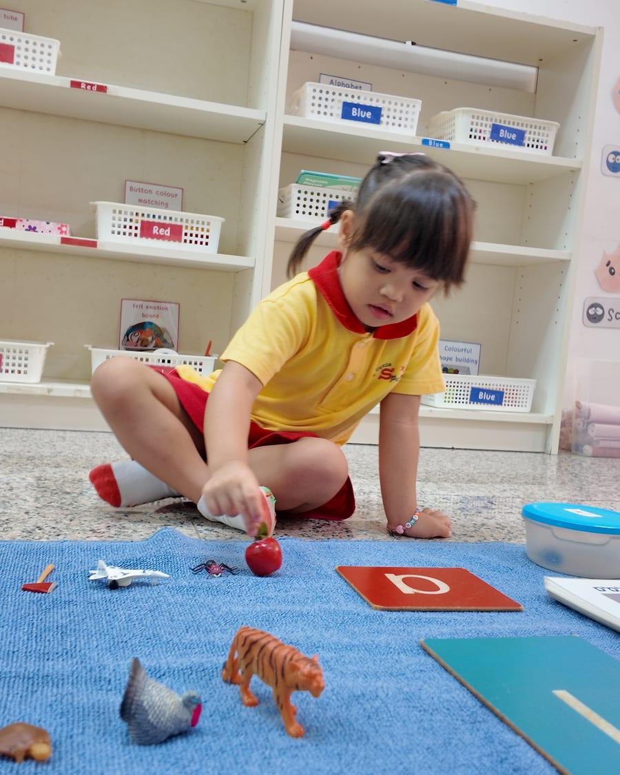 A child matching objects to a sandpaper letter during a Montessori phonics activity